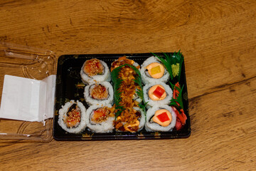 Set of sushi rolls in plastic box on wooden table. Sushi for take away or delivery of sushi in plastic container