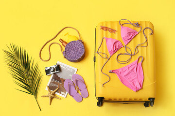 Composition with suitcase, photo camera, swimsuit and beach accessories on yellow background