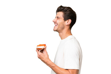 Young caucasian man holding sashimi over isolated background laughing in lateral position