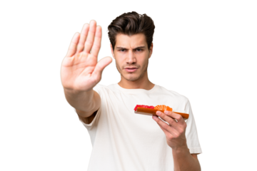 Young caucasian man holding sashimi over isolated background making stop gesture