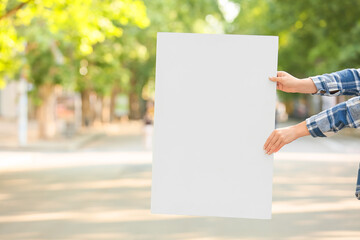 Female hands holding blank poster on city street