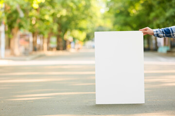 Female hand holding blank poster on city street