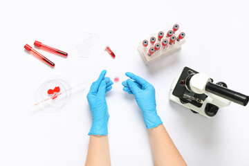 Hands of female scientist with modern microscope, blood samples and petri dish on white background