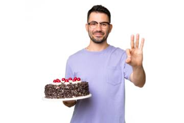 Young caucasian man holding birthday cake isolated on green chrome background happy and counting three with fingers