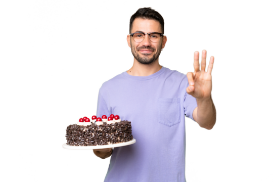 Young caucasian man holding birthday cake isolated on green chrome background happy and counting three with fingers