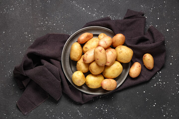 Plate with raw baby potatoes on black background