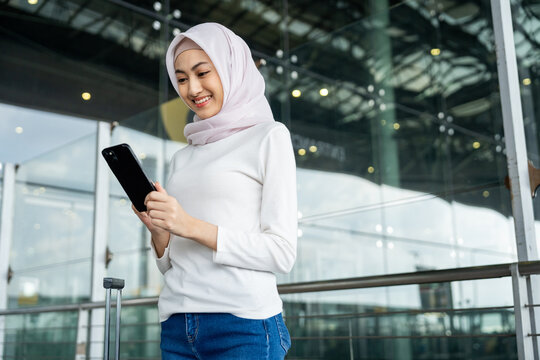 Muslim asian businesswoman traveler holding boarding pass ticket, passport and smartphone at the airport terminal with her luggage. Islamic cheerful tourist female having holiday trip weekend.