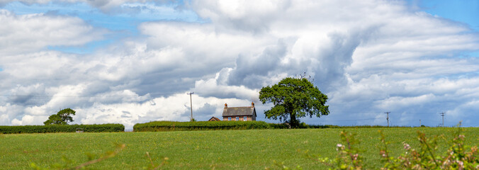 Cumulus clouds form over a solitary house giving a sense of huge scale. Wide panoramic. Strong...