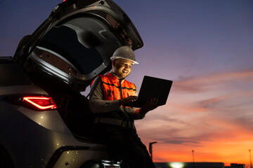 Smart engineer wearing safety uniform working with laptop sitting back of the car near airport at...