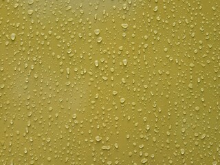 Close-up of water droplets on a smooth yellow surface after rain with scattered patterns