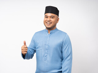 Portrait happy young asian muslim man standing thumbs up on isolated white background. Islamic Attractive Muslim man wearing songkok cap islam costume.