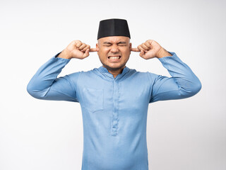 Angry boring young asian muslim man headache stressed and frustrated covering his ears with hands due to loud noise. Annoyed noise sound pollution blocking ears. Islam wearing songkok muslim costume