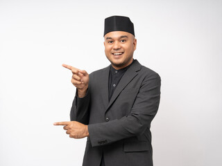 Portrait happy young asian muslim man pointing on isolated white background. Islamic Attractive Muslim man wearing songkok cap islam costume.