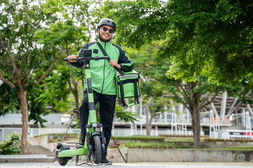 Rider food delivery man wearing green uniform and helmet ride the EV scooter delivery food service to customer. Happy delivery man with green backpack shipping of goods to customers by scooter