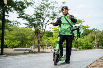 Rider food delivery man wearing green uniform and helmet ride the EV scooter delivery food service to customer. Happy delivery man with green backpack shipping of goods to customers by scooter