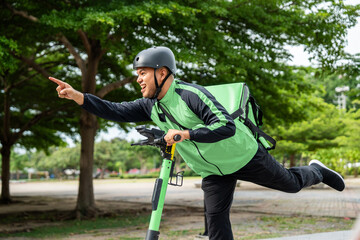 Rider food delivery man wearing green uniform and helmet ride the EV scooter delivery food service to customer. Happy delivery man with green backpack shipping of goods to customers by scooter