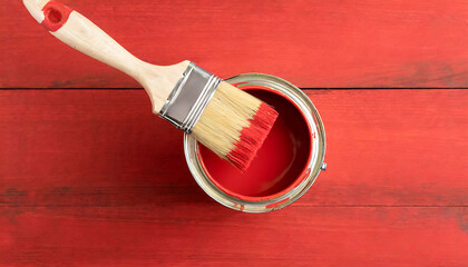 A paint can with a brush in it is sitting on a red background. Scene is cheerful and creative, as it suggests someone is about to start a painting project