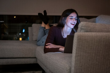 Fototapeta premium Young woman alone at home working late at night on her laptop. Freelancing, studying, chatting online or trying to meet a deadline—an intimate and real portrayal of modern life after dark