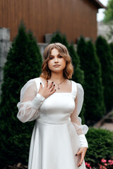 Girl in white dress on street in summer, green bushes behind her