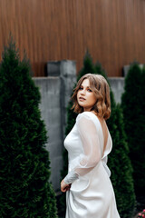 Girl in white dress on street in summer, green bushes behind her
