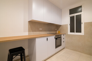 Modern kitchen side view with white cabinets, wood counter, oven and a single black bar stool