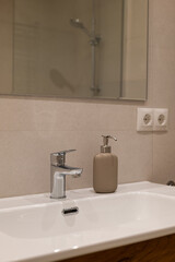 Minimalist bathroom sink area with chrome faucet and beige soap dispenser against neutral tiled wall