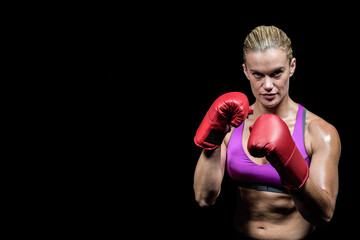 Woman posing in guard stance in studio with sports bra and red boxing gloves, copy space