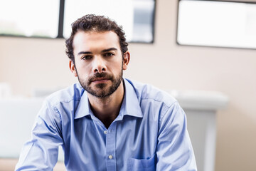 Man sitting on chair in modern office wearing light blue dress shirt near large windows