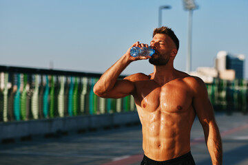 Muscular athlete drinking water after intense workout outdoors