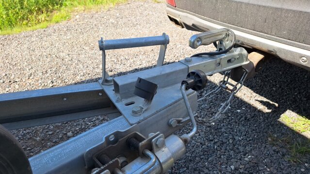 Close-up of metal trailer hitch attached to car on gravel surface