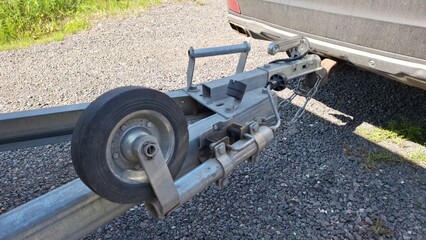 Close-up of boat trailer hitch mechanism on gravel with dusty vehicle background