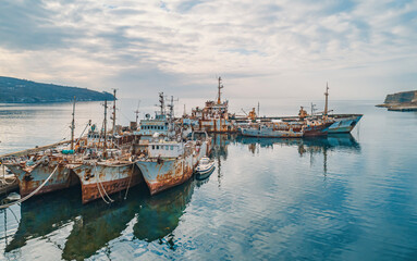 Abandoned vessels docked at a quiet harbor under a cloudy sky in early morning light
