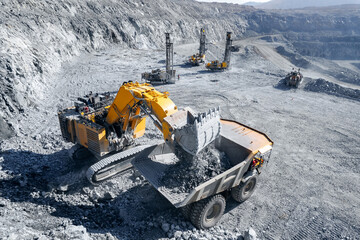 Aerial top view Open pit mining industry. Industrial excavator loading ore into big yellow truck of...