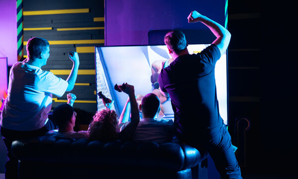 Diverse group of young adults play esports game on console in exciting team experience, back view