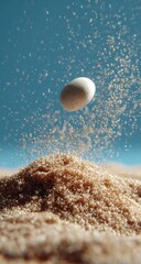 A white sphere rising above a mound of light brown granules, suspended in mid-air, surrounded by a fine spray