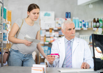 Fototapeta premium Experienced male pharmacist and a young woman are searching for information on the Internet about new drug