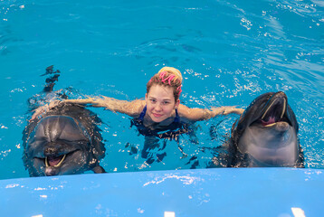 Woman interacts with dolphins in a blue pool during a marine park encounter