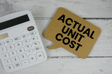 Actual Unit Cost text with calculator on wooden background
