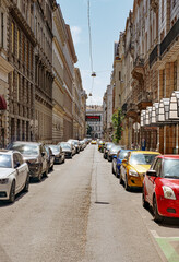 Fototapeta premium Urban street with parked cars and historic buildings on both sides, leading toward a theater sign in Budapest.