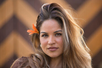 Portrait of beautiful young blonde woman with an orange flower in her hair. The woman stares at the...