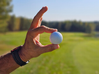 Golf ball being held up against a clear blue sky on a golf course