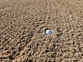 Golf ball nestled in sand trap on golf course