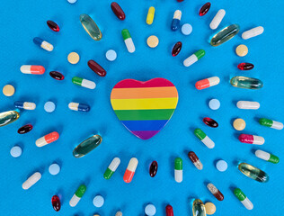 A vibrant heart shape in rainbow colors sits at the center, surrounded by assorted capsules and pills, illustrating the connection between health