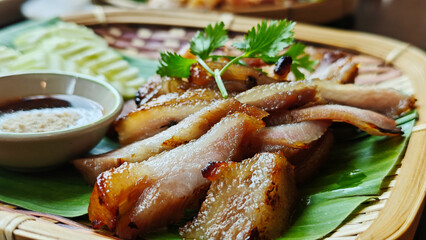 Grilled pork neck served with dipping sauce on a bamboo plate