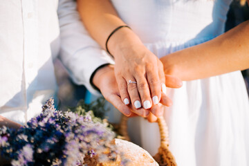 Couple holding hands with engagement ring and flowers at sunset
