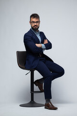 Spanish Man in Blue Suit Sitting on Stool with Arms Crossed