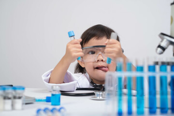 A young child wearing a lab coat and goggles conducts a playful science experiment with test tubes...