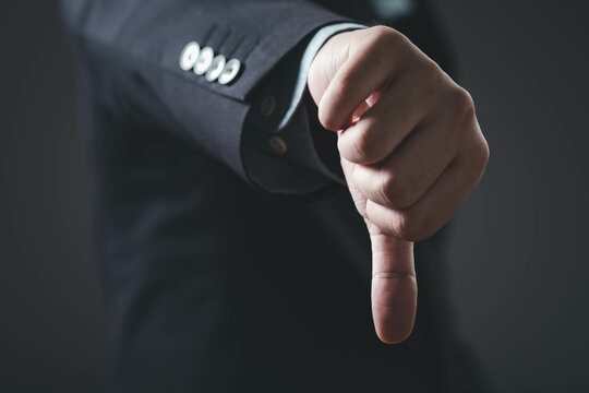 A business professional shows a thumbs-down gesture, indicating disapproval or negativity in a formal setting.