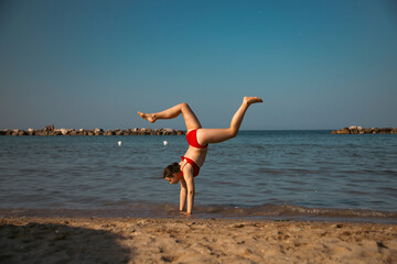 Energetic teenager girl doing handstand on the beach
