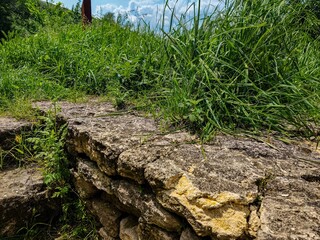 A rock wall with a grassy area in between. The grass is green and the rock wall is brown